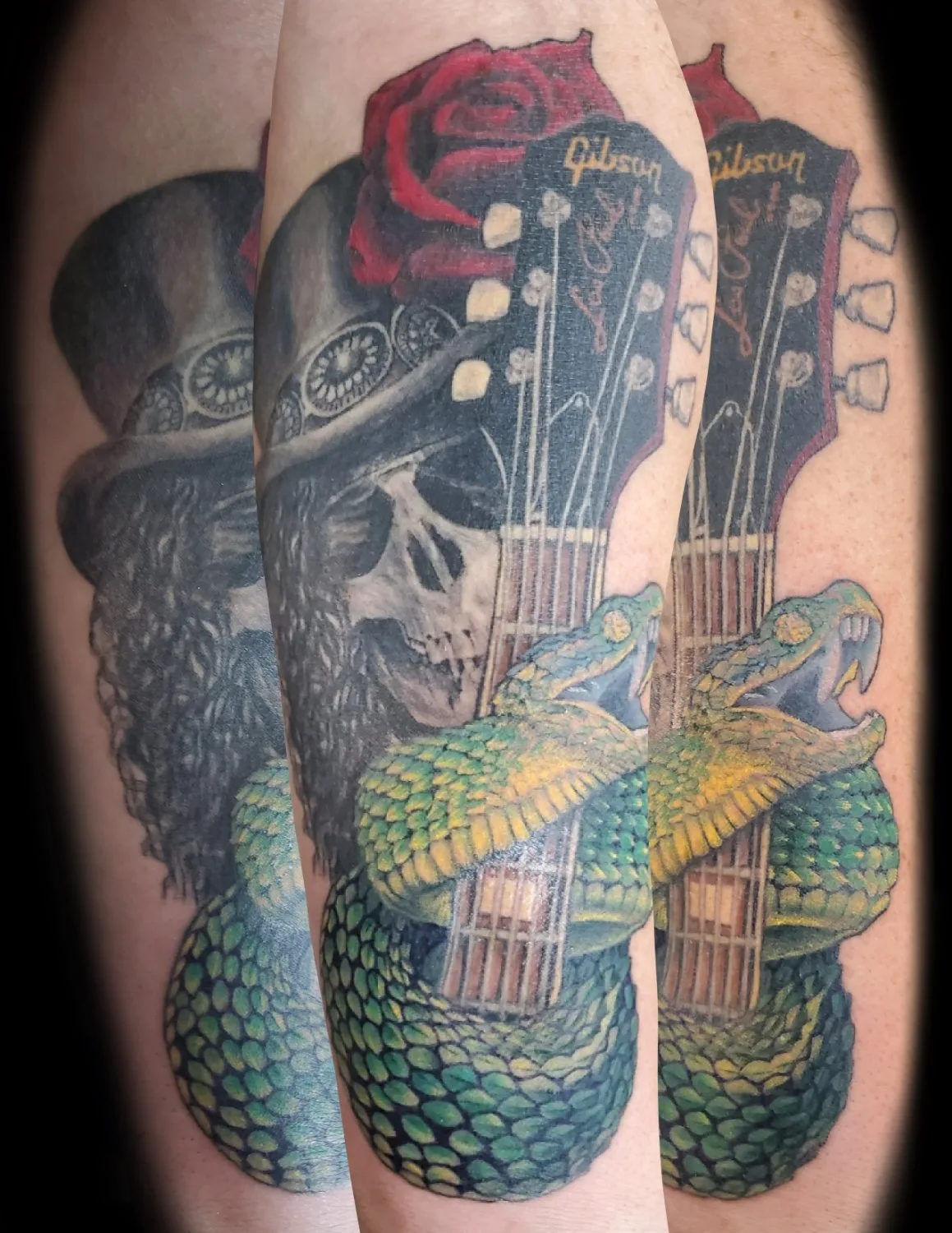 A realistic tattoo of a skull wearing a top hat, coiled with a detailed green and yellow snake around a black Gibson Les Paul guitar, with a deep red rose at the headstock, rendered in dark tones with vibrant colour accents.