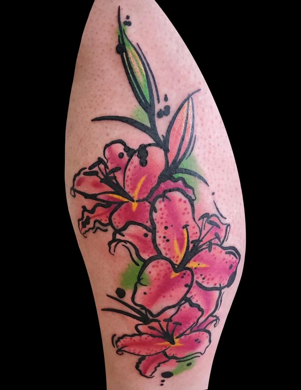 A tattoo of pink lilies with bold black outlines and watercolour-style colour washes, accented by loose green foliage splashes and scattered black dots, arranged in a vertical cascade on an arm.