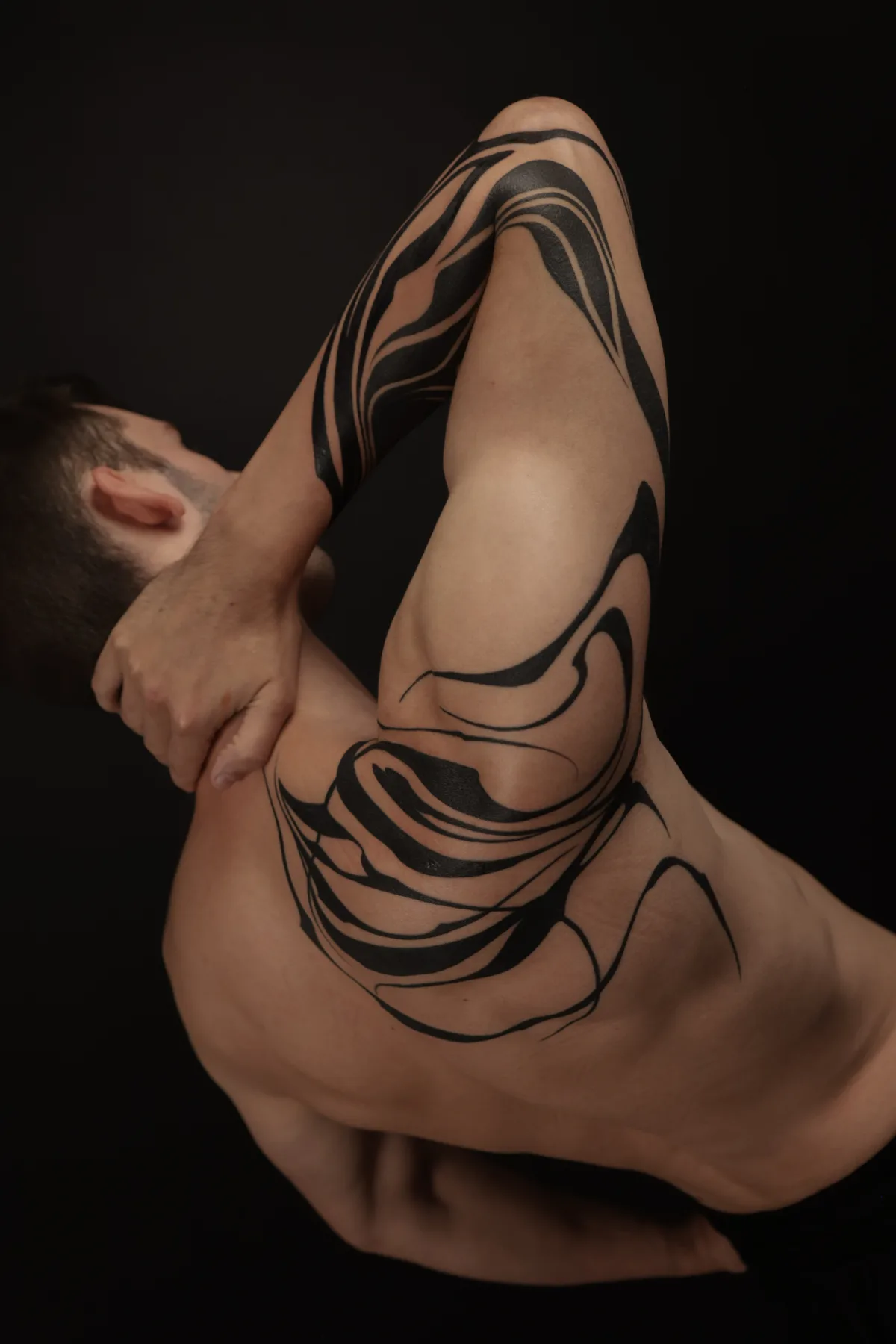 Thor Keilitz's shoulder and arm tattoo features thick flowing black shapes interlaced with fine swirling lines, creating abstract calligraphy-like design that accentuates the musculature.