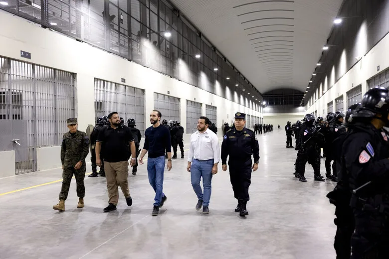 President of El Salvador Nayib Bukele (center, in a dark blue jacket) together with Defense Minister Rene Merino Monroy (far left) and Police Chief Mauricio Arriaza (in black uniform) inspect the new CECOT prison complex in January 2023. Guard units are lined up on both sides. Photo: Casa Presidencial El Salvador (CC0).