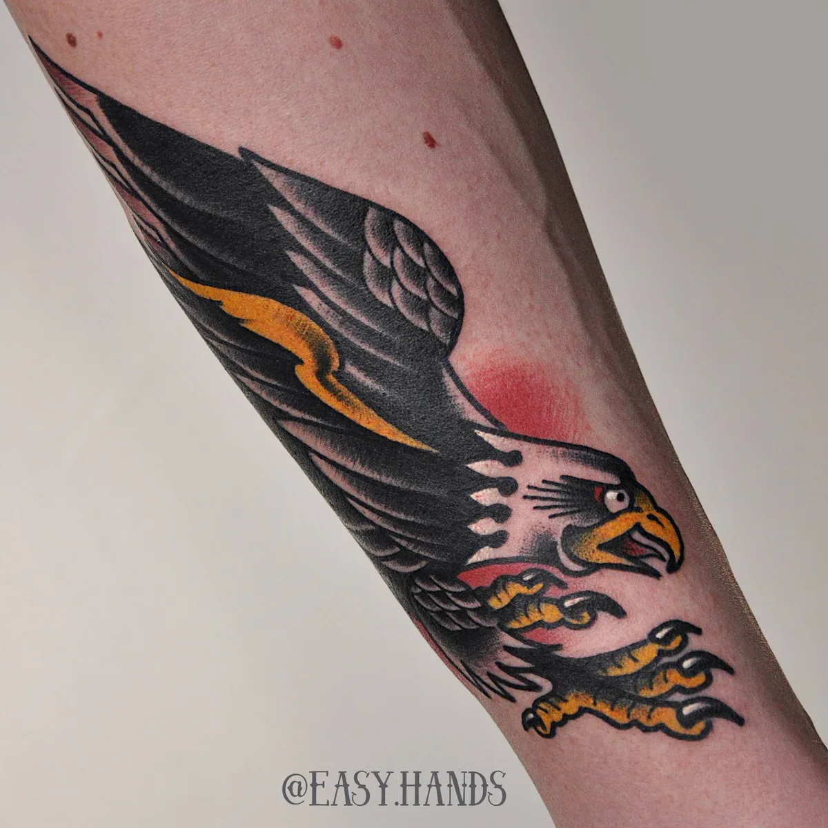 Traditional style tattoo of an eagle in flight with bold black outlines and a limited color palette of red, yellow, and blue.