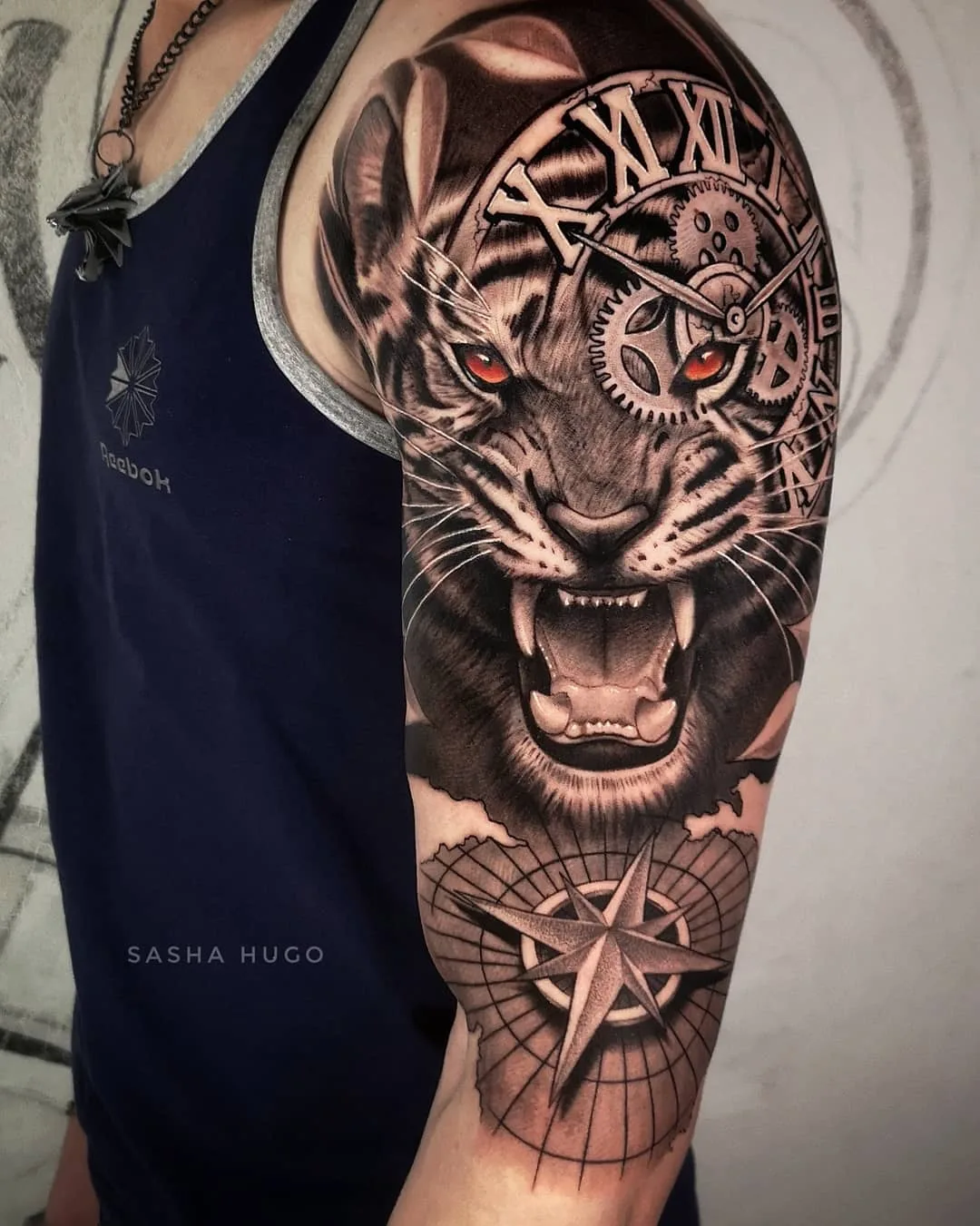 A detailed black and grey forearm tattoo featuring a roaring tiger with a clock incorporated into its design and a compass below.