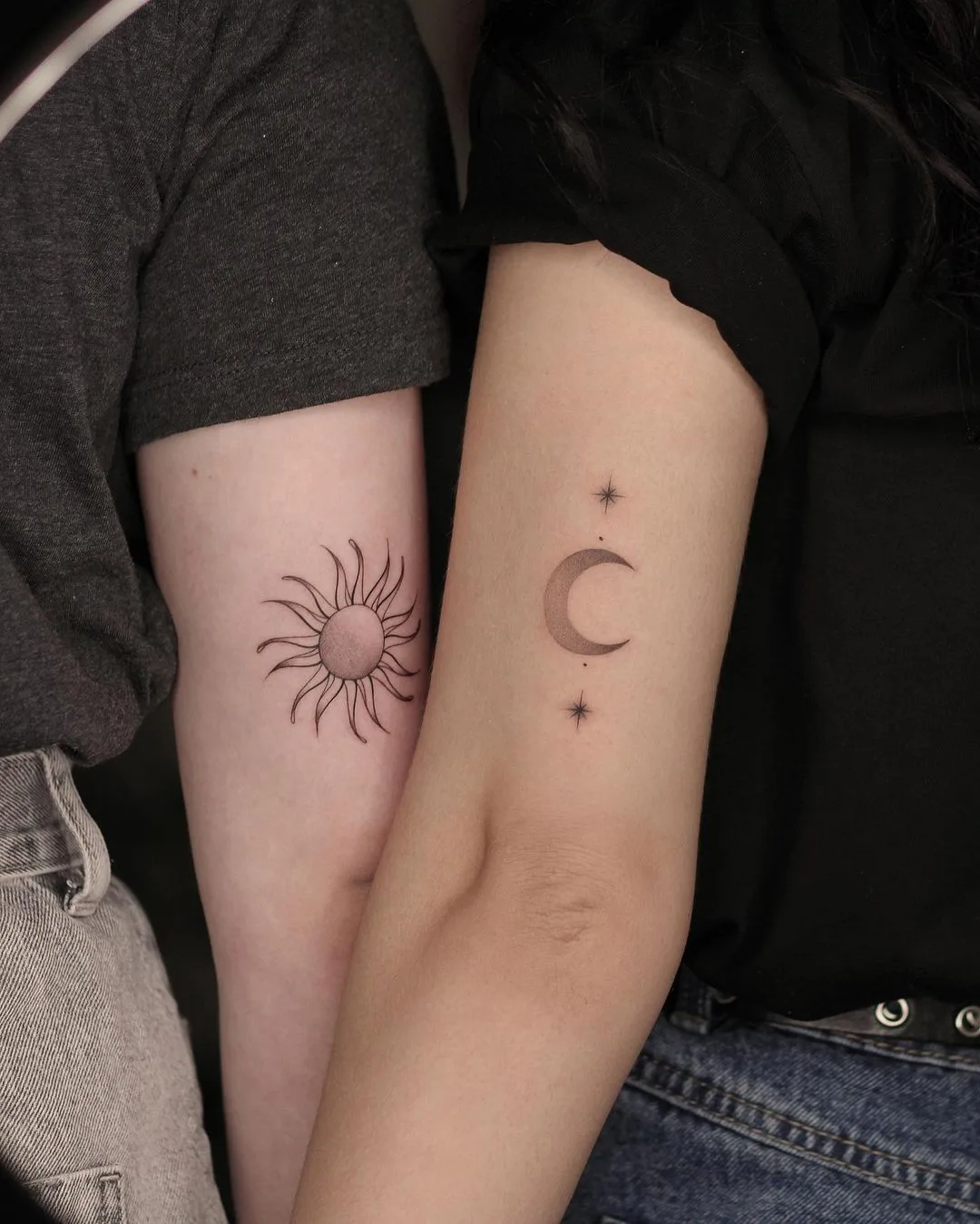Two matching tattoos shown together, each depicting a sun and a crescent moon surrounded by small stars. Executed in a delicate fine-line style with thin black outlines.