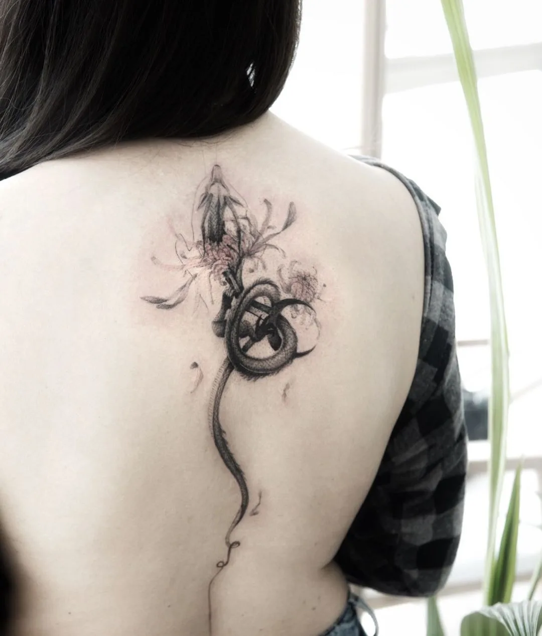 Tatouage délicat noir et gris représentant un serpent entrelacé avec des fleurs, réalisé dans un style esquisse fine line.