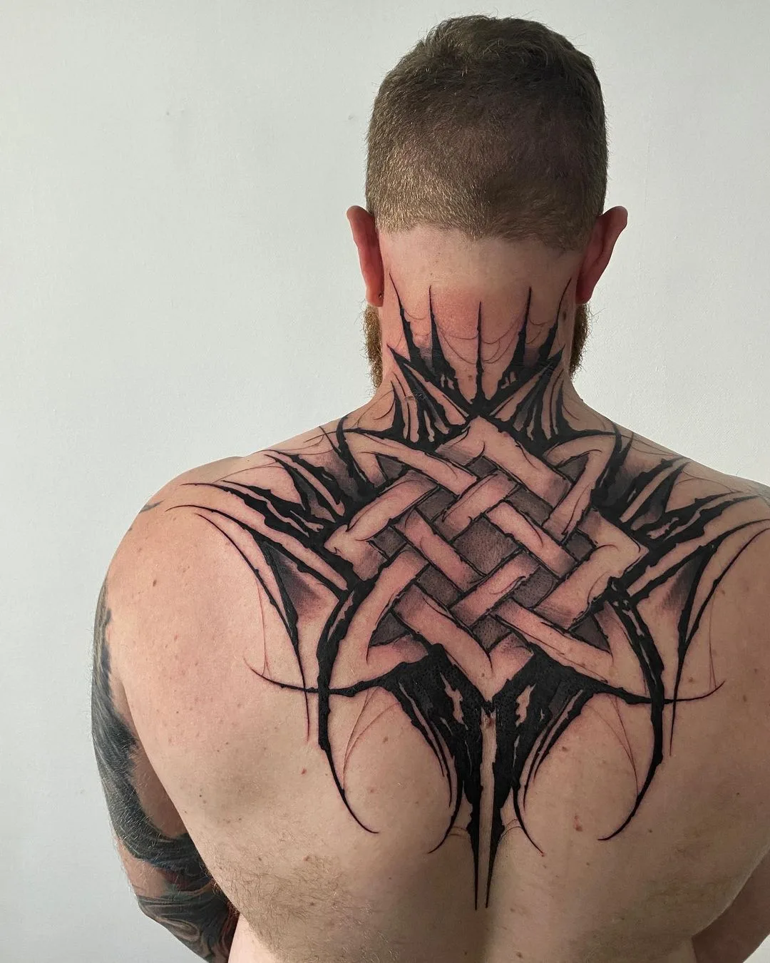 Ein großes Blackwork-Tattoo auf dem oberen Rücken mit einem geometrischen Knotendesign und kantigen Elementen sowie Schattierungen für Tiefe.