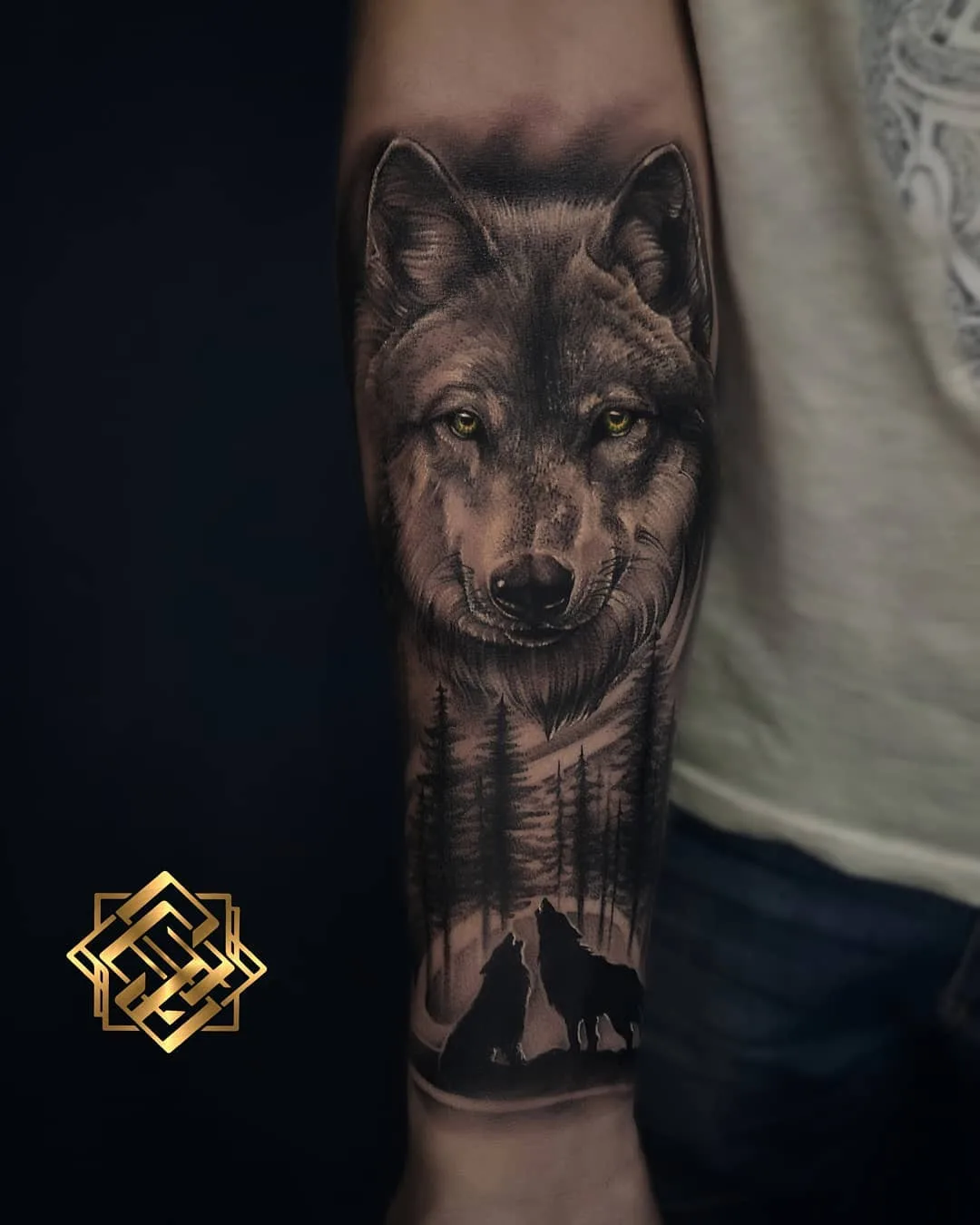 A detailed black and grey tattoo of a wolf's face with a forest scene below. The tattoo is well-executed with realistic shading and detail.