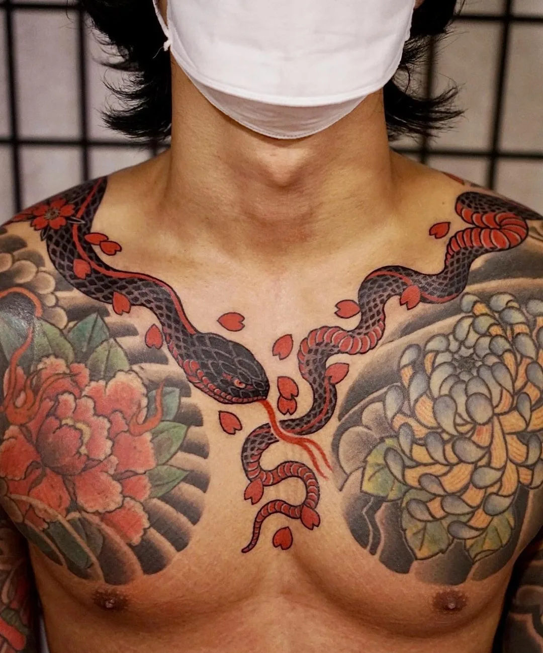 A vibrant Japanese-style tattoo featuring a snake intertwined with flowers and petals spread across the chest, in traditional irezumi composition.