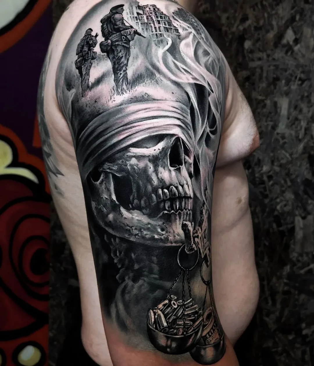 A detailed black and grey tattoo depicting a blindfolded skull, soldiers in the background, and a scale holding bullets.