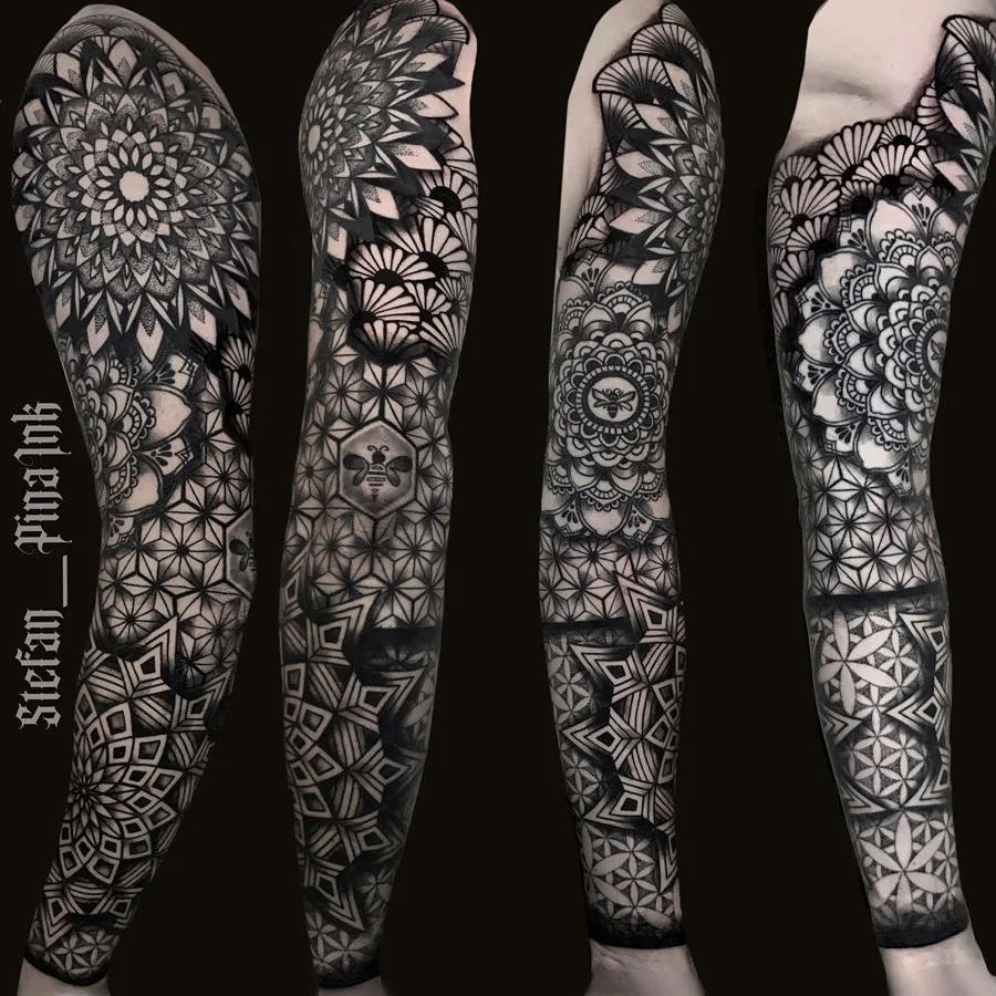 A complex black and grey full sleeve tattoo combining geometric patterns, mandala designs, and a bee motif, with precise linework and intricate symmetrical structures covering the entire arm.
