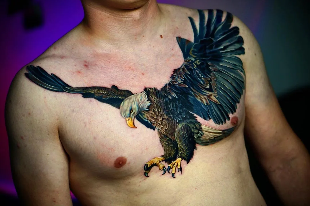 Realistic chest tattoo of an eagle with wings spread wide, featuring detailed feather shading and color blending across the pectorals.