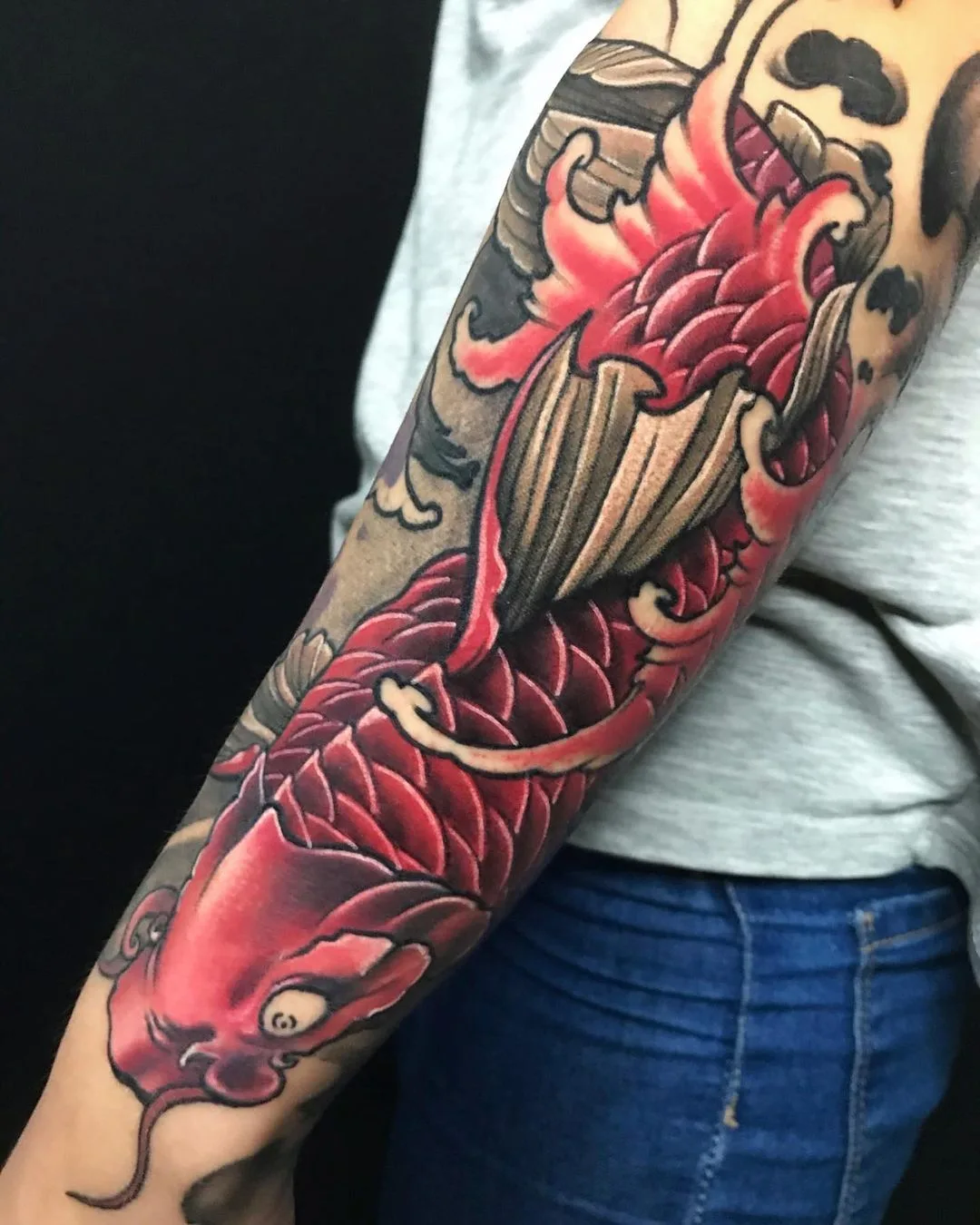 A full sleeve tattoo featuring a large red koi fish swimming through detailed Japanese-style waves in vivid colour.