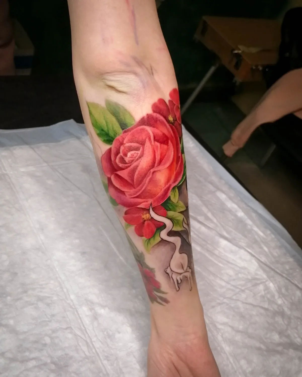 Ein lebhaftes, realistisches Tattoo mit einer großen roten Rose und anderen Blumen mit detaillierten Schattierungen und Highlights.