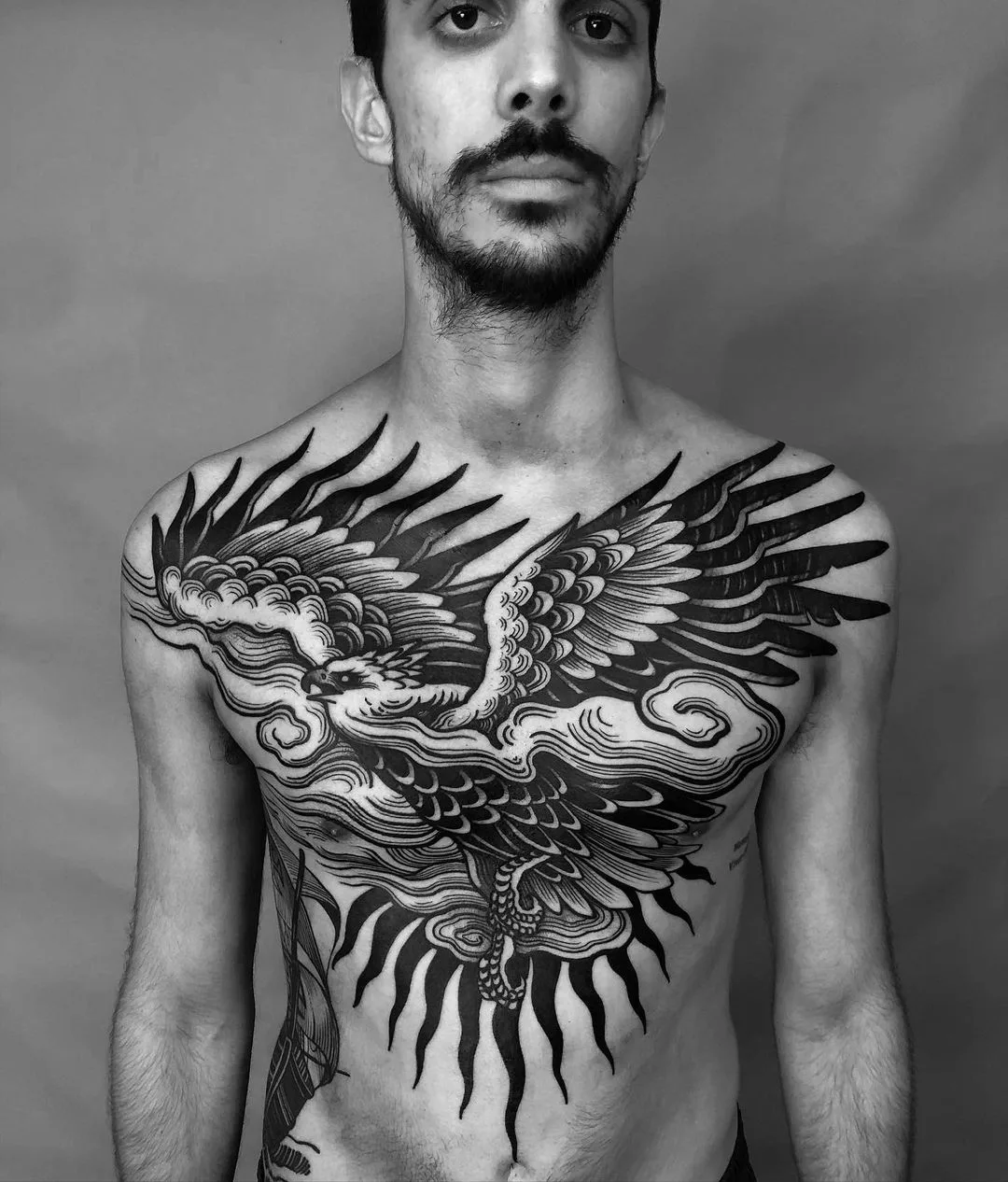 Large blackwork tattoo of an eagle with spread wings against a backdrop of stylized clouds and sun rays, using bold black fills.