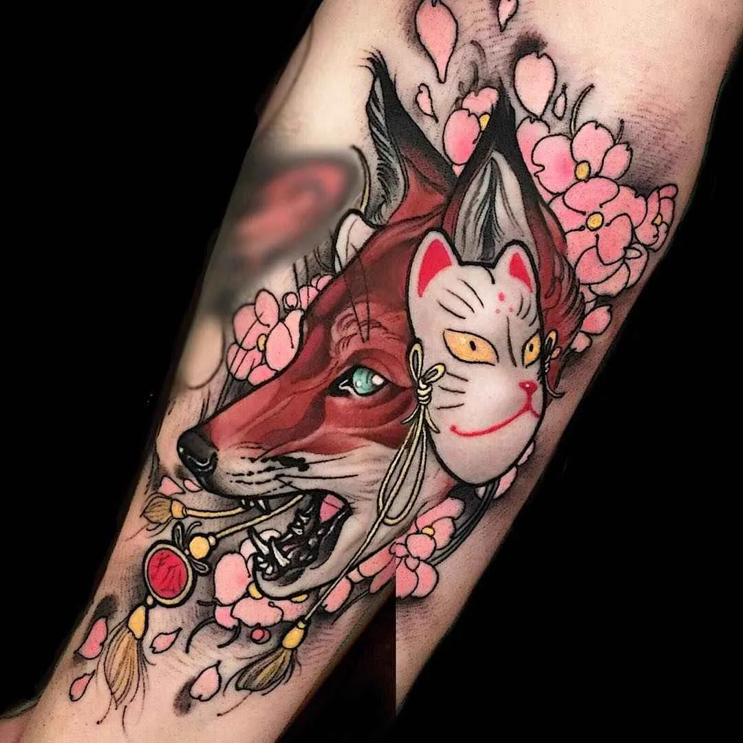 A colourful tattoo of a fox wearing a mask surrounded by cherry blossoms, combining Japanese and illustrative styles.