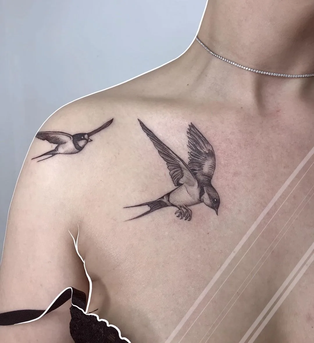 Tatouage délicat de deux hirondelles en vol, réalisé en noir et gris avec un style fine line.