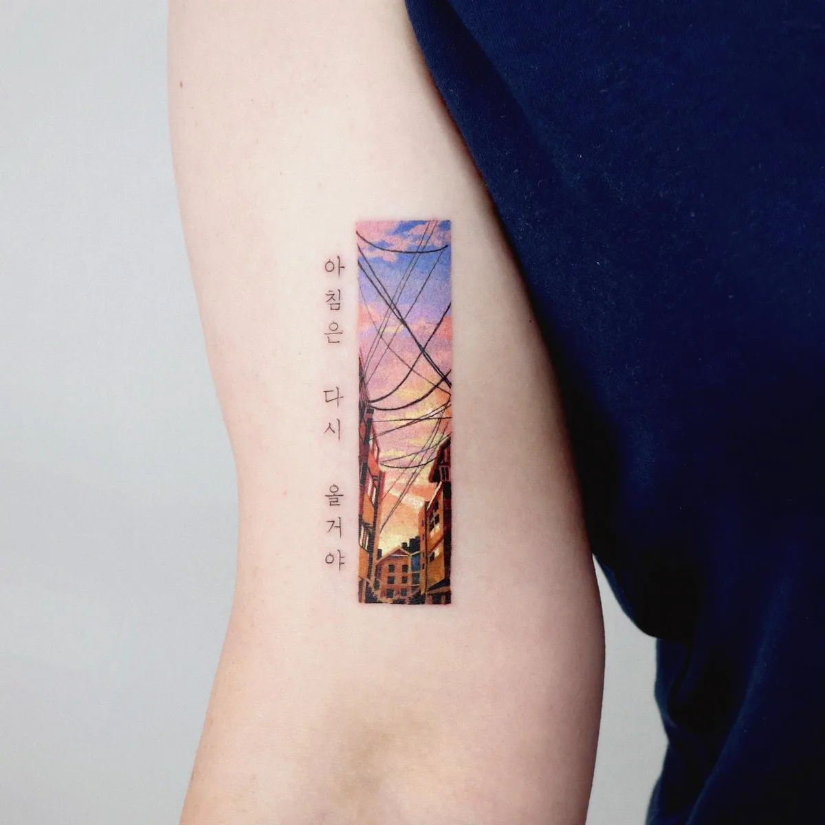 A colorful cityscape tattoo featuring a vibrant sunset, buildings, and Korean text.