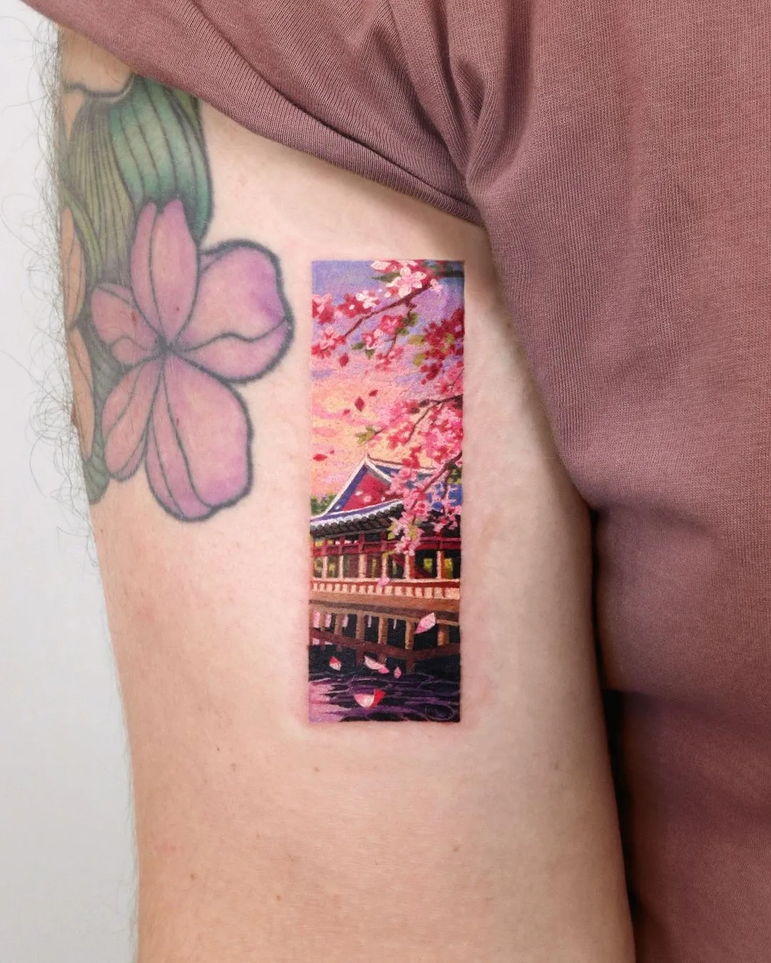 A vibrant realistic tattoo depicting a traditional Japanese building surrounded by cherry blossoms reflected in water.