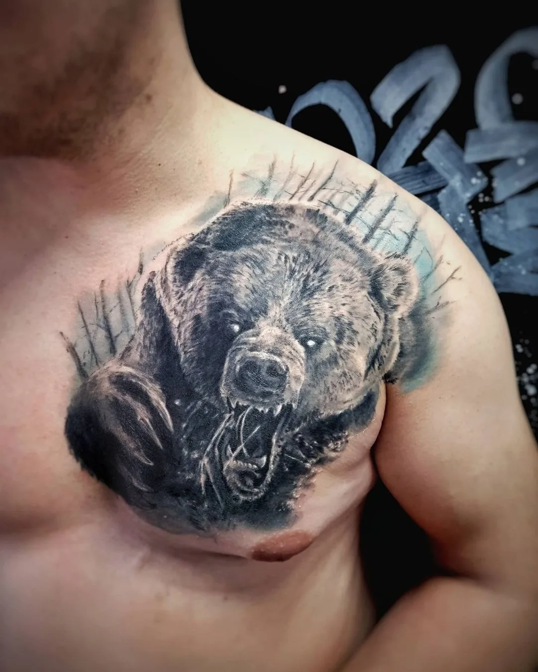 A detailed black and grey tattoo of a snarling bear on the chest with realistic shading and texture.