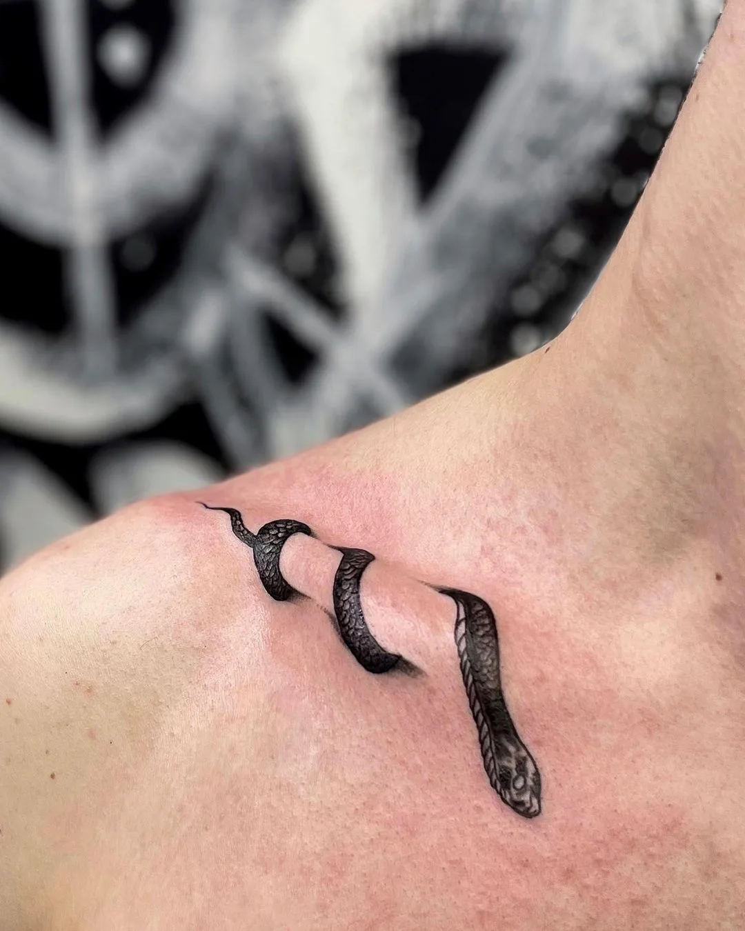 Tatouage réaliste d'un serpent noir semblant émerger de la peau, créant un effet tridimensionnel.