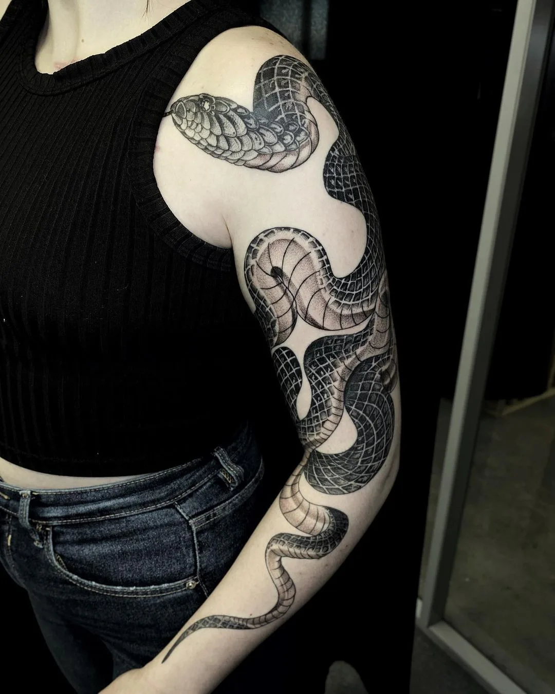 Tatouage blackwork détaillé d'un serpent enroulant le bras, incorporant des motifs géométriques et un ombrage en pointillé.