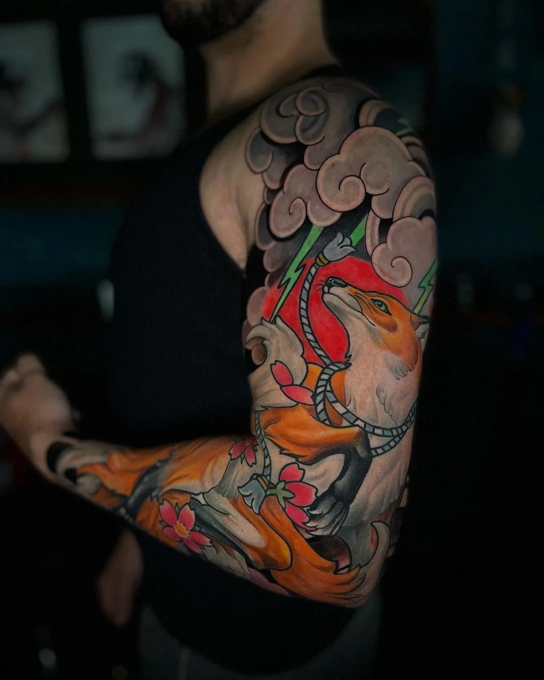 A vibrant full-sleeve tattoo in Japanese style depicting a fox among clouds and cherry blossoms, covering the entire arm.