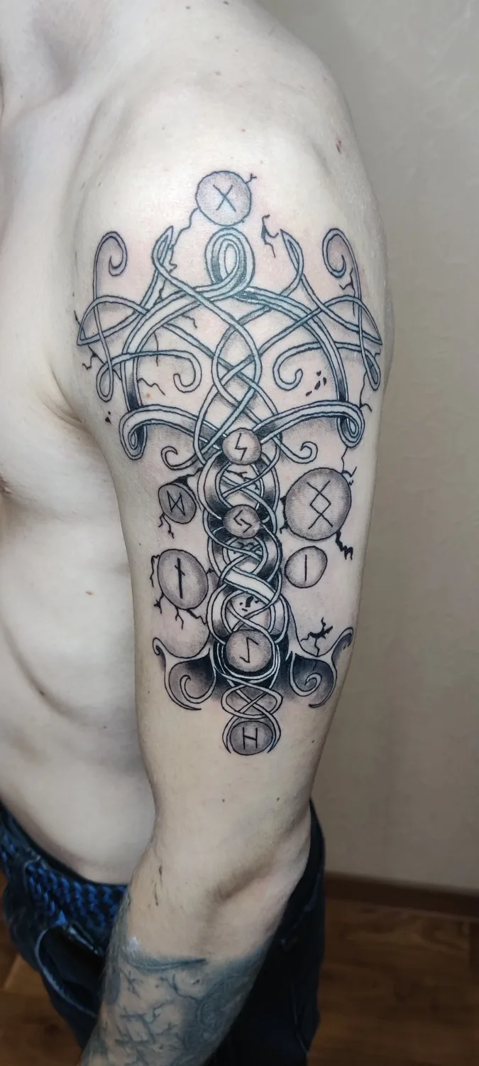 Tatouage en noir et gris avec entrelacs celtiques et runes, placé sur l'épaule et le haut du bras.