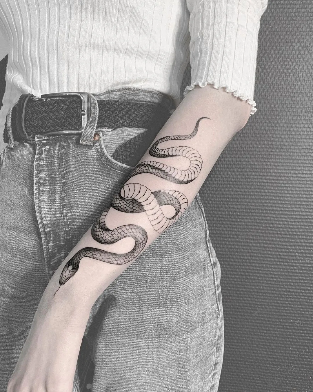 A detailed black and grey snake tattoo wrapping around the forearm, executed in a linework style with careful shading to define the scales.