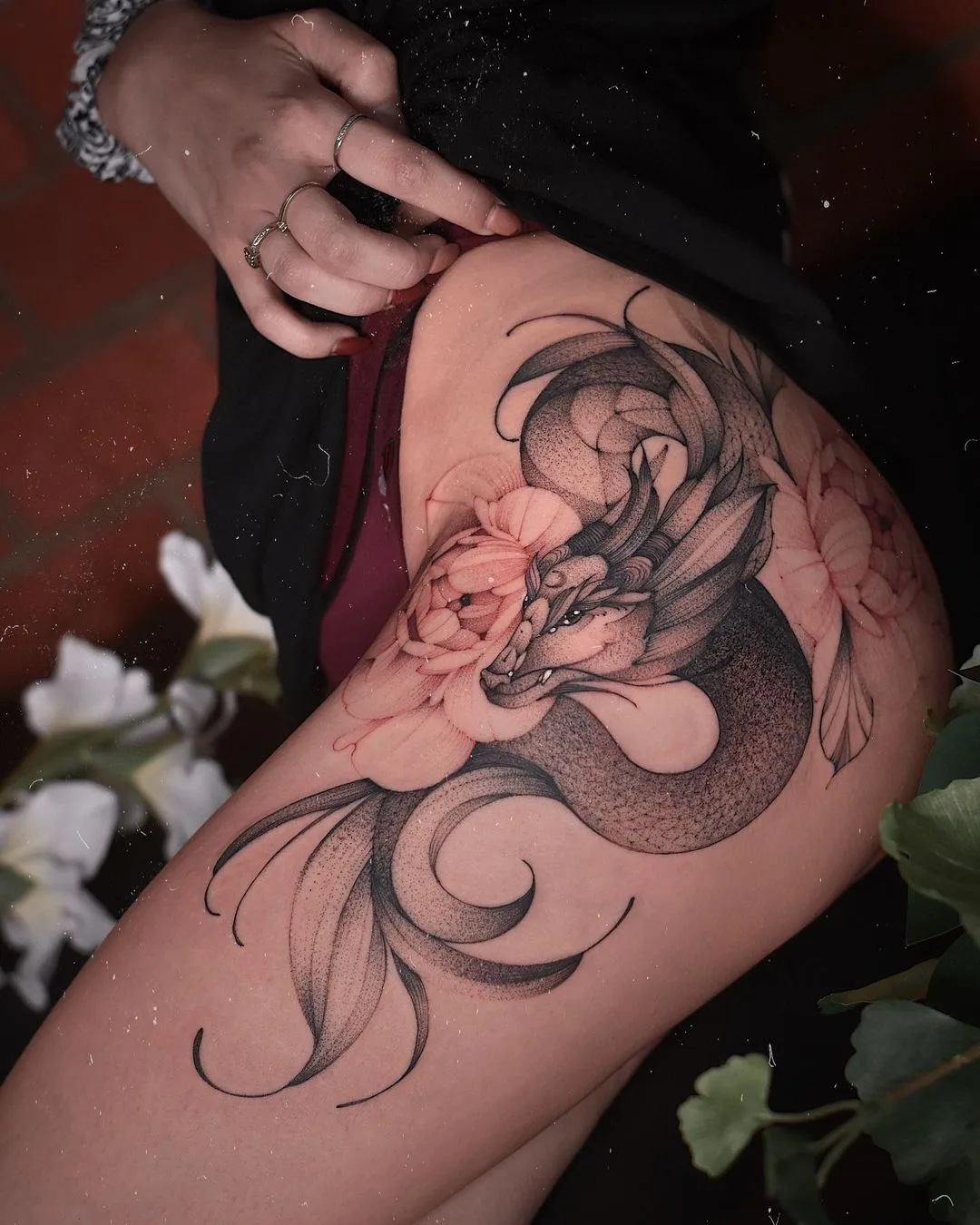 Tatuagem preta na coxa com dragão e flores