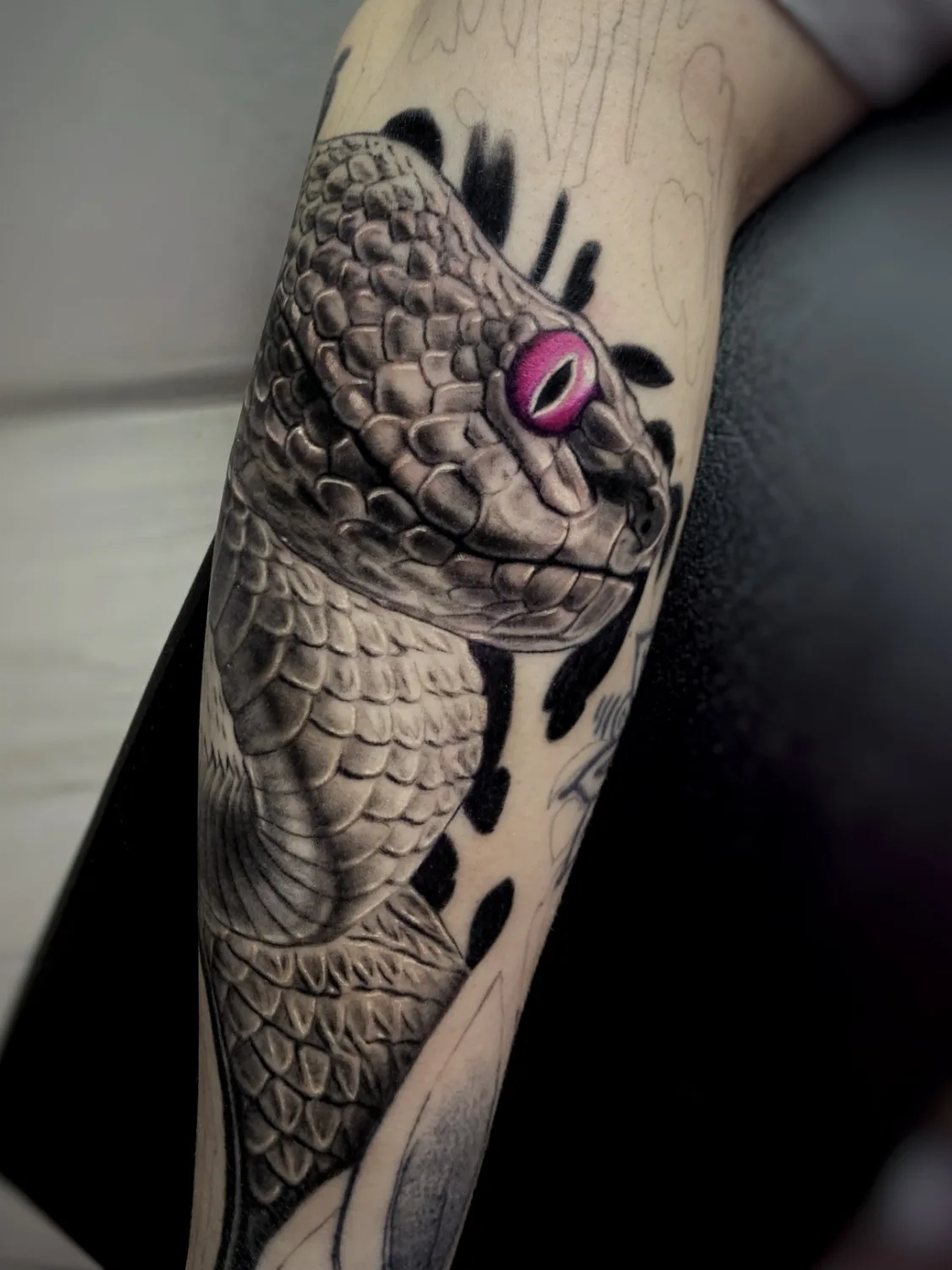 A highly realistic black and grey tattoo of a snake or dragon with its mouth open, showcasing precise scale detail and dramatic shading.