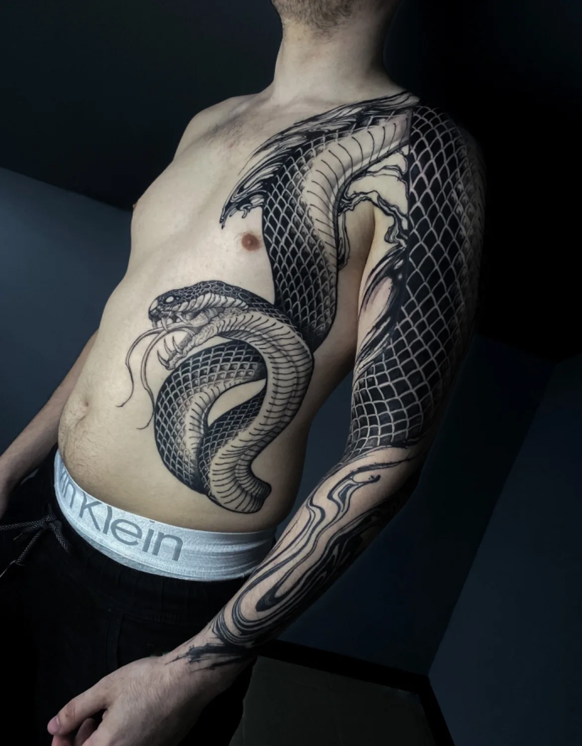 Großformatiges Blackwork-Tattoo einer Schlange, die sich um Torso und Arm windet, mit detaillierter Linienführung und Schattierung.