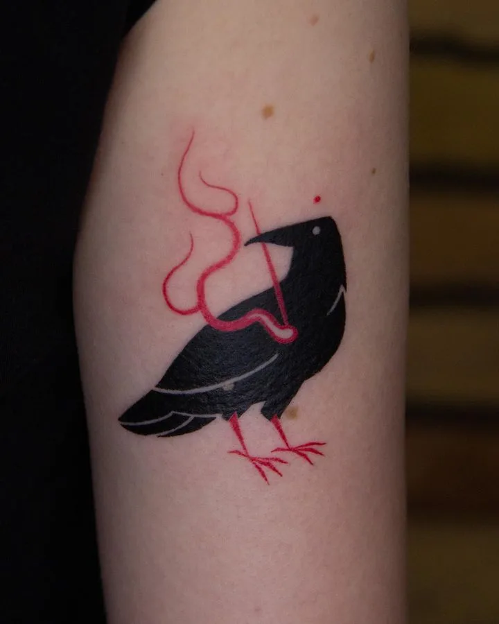 A blackwork forearm tattoo of a crow rendered in solid black ink, holding a red curved line that arcs upward, combining clean line and minimal colour.