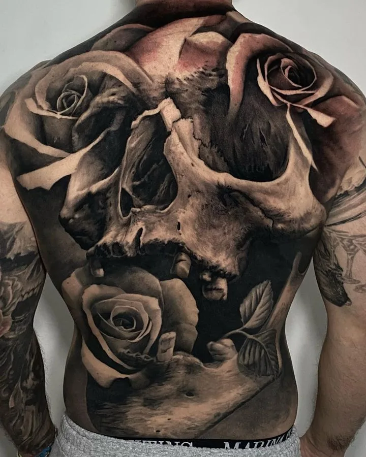 A large, detailed black and grey tattoo featuring a skull surrounded by roses, covering the entire back.