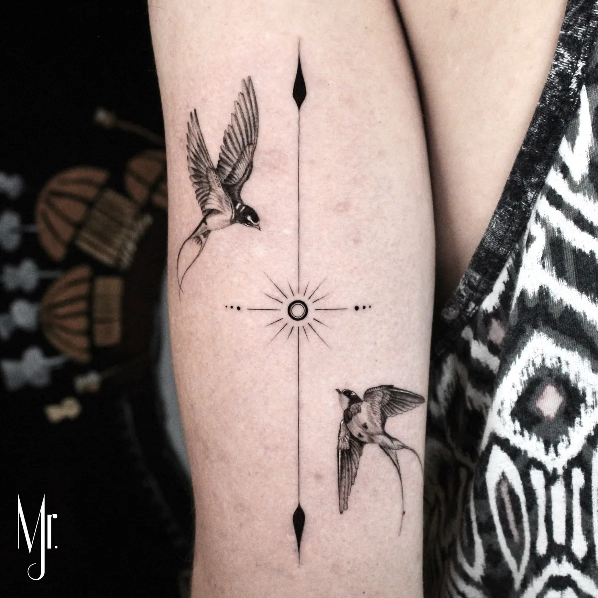 Tatuaggio fine line con due rondini in volo e una bussola, realizzato con linee sottili e precisione geometrica.