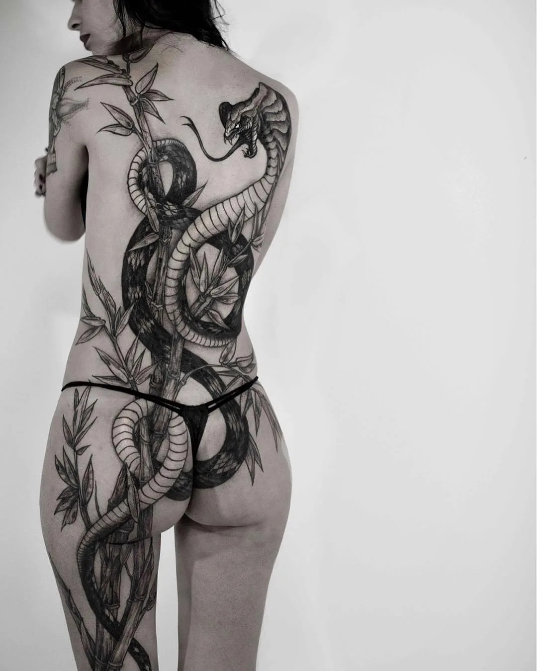A large blackwork tattoo of a snake coiled around bamboo stalks, covering the entire back with bold black masses and negative space.