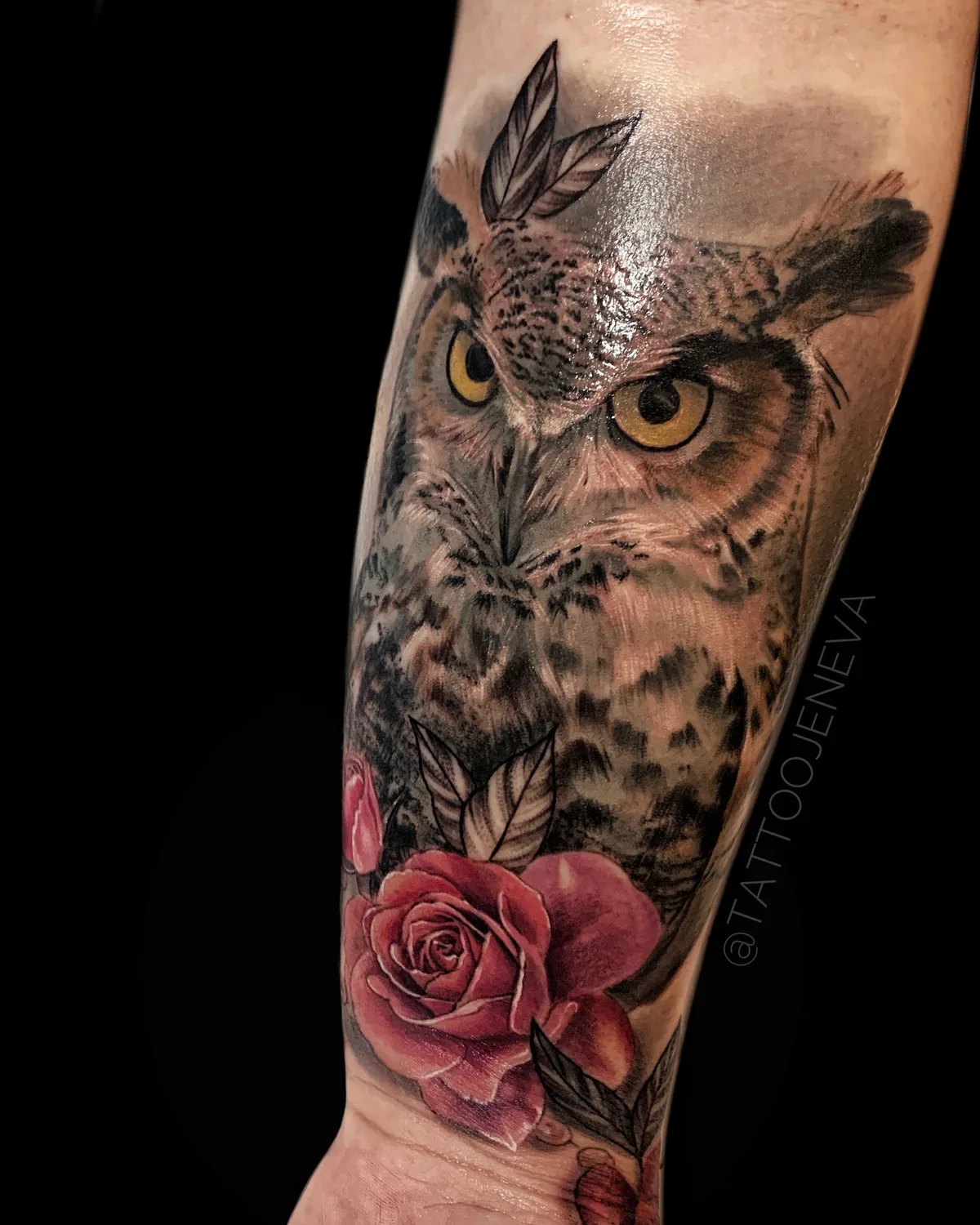 A detailed black and grey owl tattoo featuring yellow eyes and a red rose at the base, rendered in realistic style.
