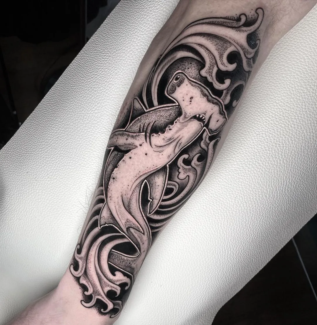 A detailed black and grey dotwork tattoo of a hammerhead shark swimming through stylised waves, using stippling to create depth and texture.