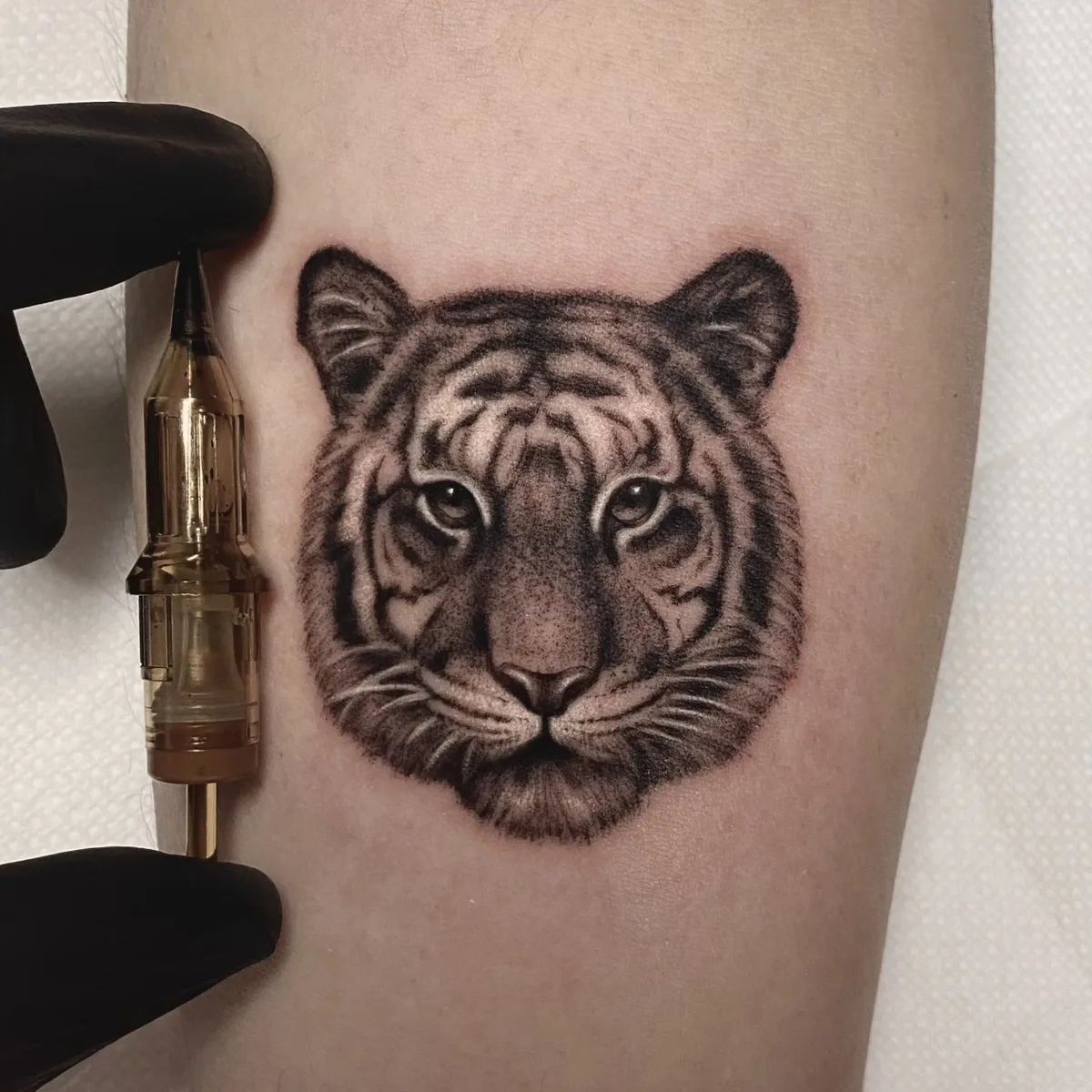 This is a detailed black and grey tattoo of a tiger's face. The tattoo is done in a realistic style.
