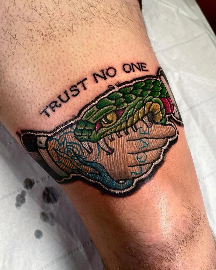 A neo-traditional tattoo of a snake biting a hand with the words 'TRUST NO ONE' lettered above, combining serpent symbolism with a pointed message.