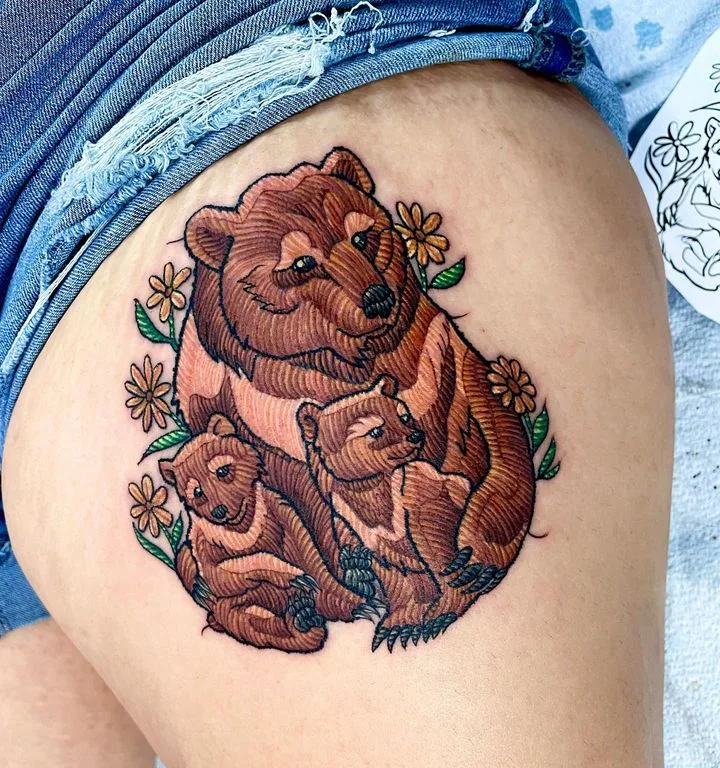 A neo-traditional tattoo featuring a mother bear and her cubs surrounded by flowers.