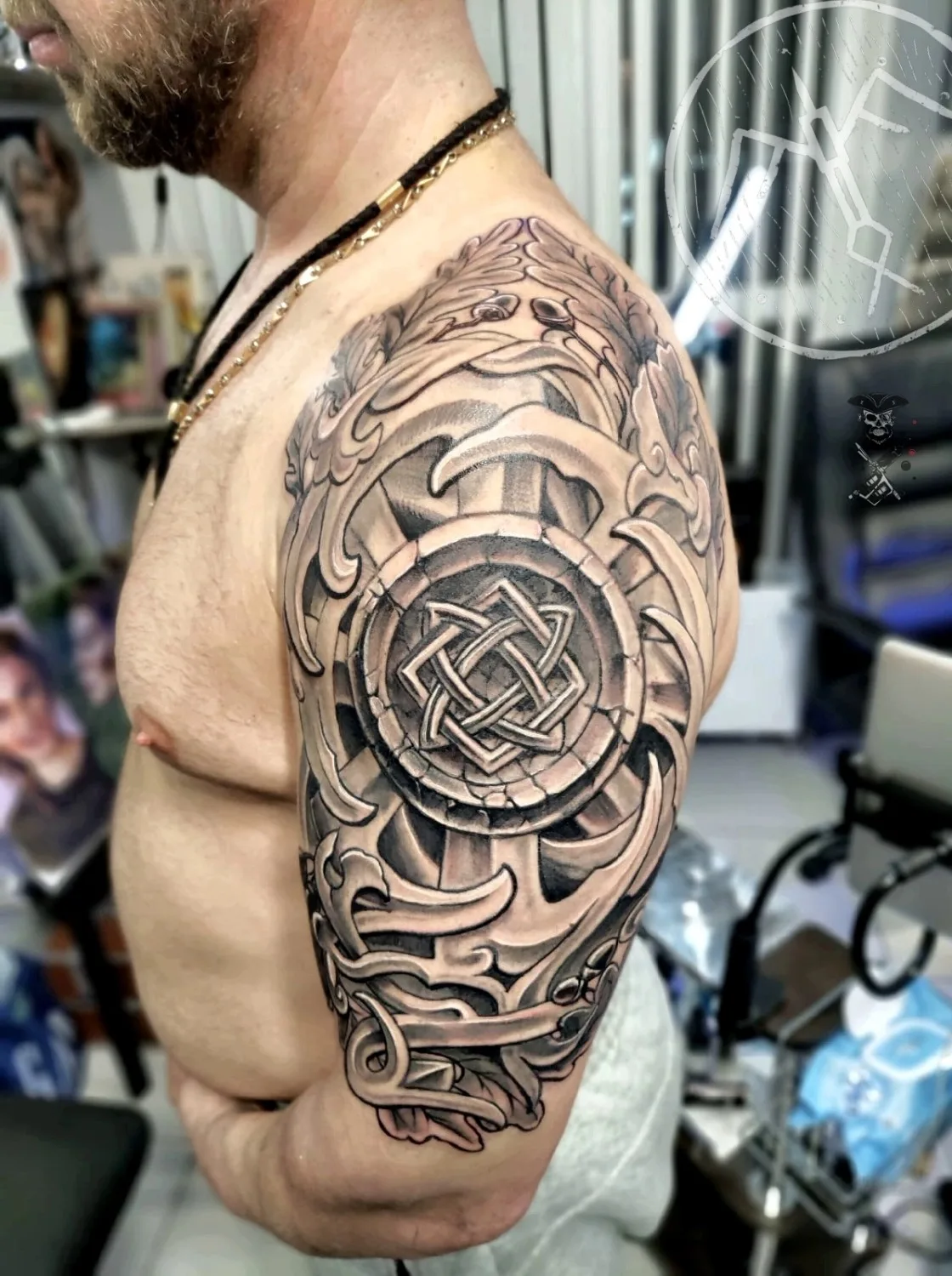 Ein schwarz-graues Tattoo mit einem keltischen Endlosknoten als Mittelpunkt, umgeben von ornamentalen Elementen.