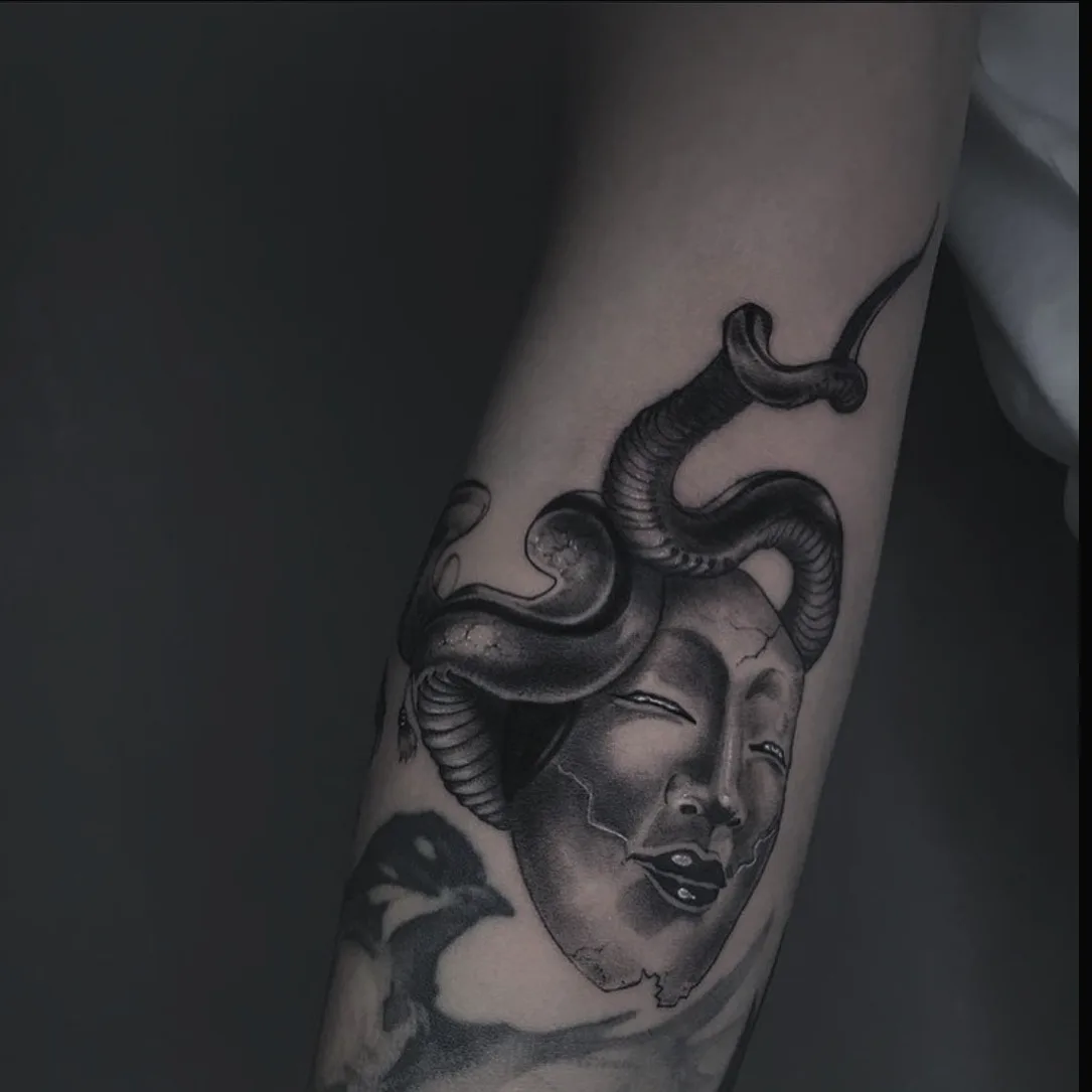 A detailed black and grey realistic tattoo depicting a face surrounded by snakes as hair, referencing the Medusa myth with careful shading and expression.