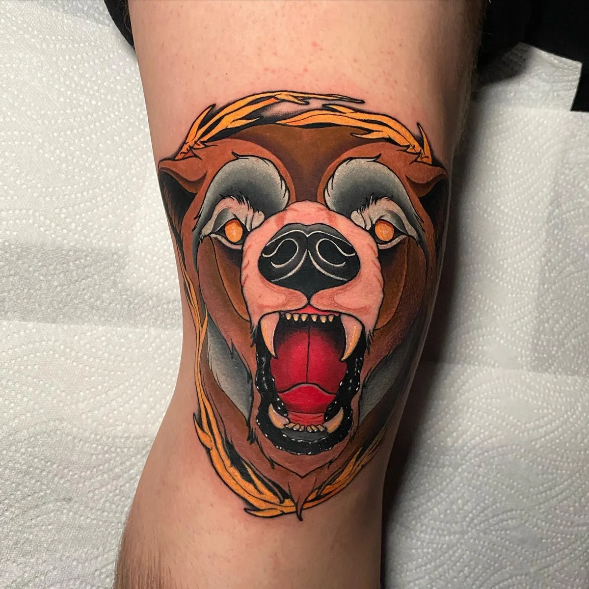 A traditional style tattoo of a bear's head with an open mouth, colourful and detailed.