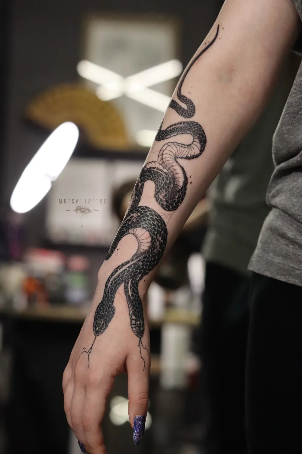 A detailed blackwork tattoo of a snake winding from the forearm down over the hand, with bold solid areas and fine linework defining the scales.
