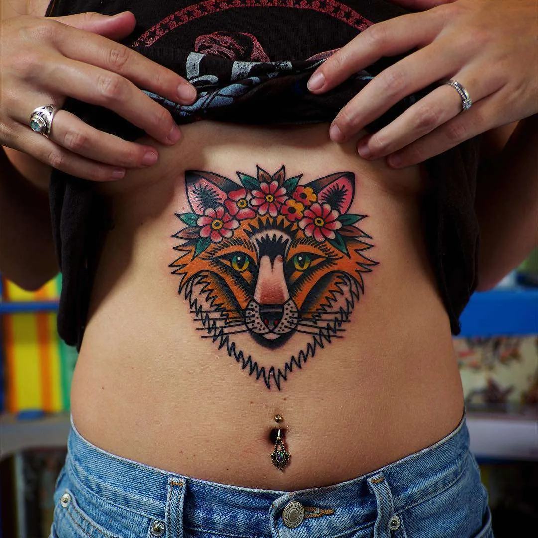 A colourful neo-traditional tattoo of a fox wearing a flower crown, placed on the stomach with bold outlines and vibrant colour.