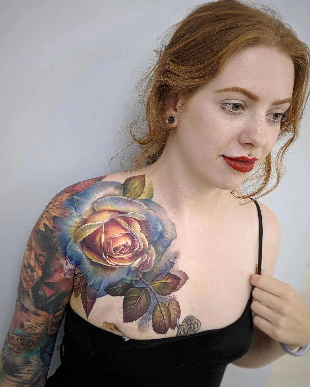 Lebhaftes Rosen-Tattoo im Aquarell-Stil mit realistischen Schattierungen auf Brust und Schulter, das sich zu einem Teilsleeve mit zusätzlichen Motiven erstreckt.