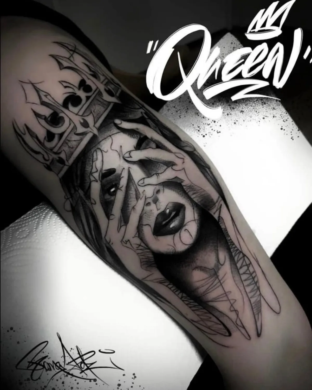 Tatuaggio in bianco e nero di un volto femminile con le mani che lo coprono e una corona, con la parola 'Queen' scritta sopra.