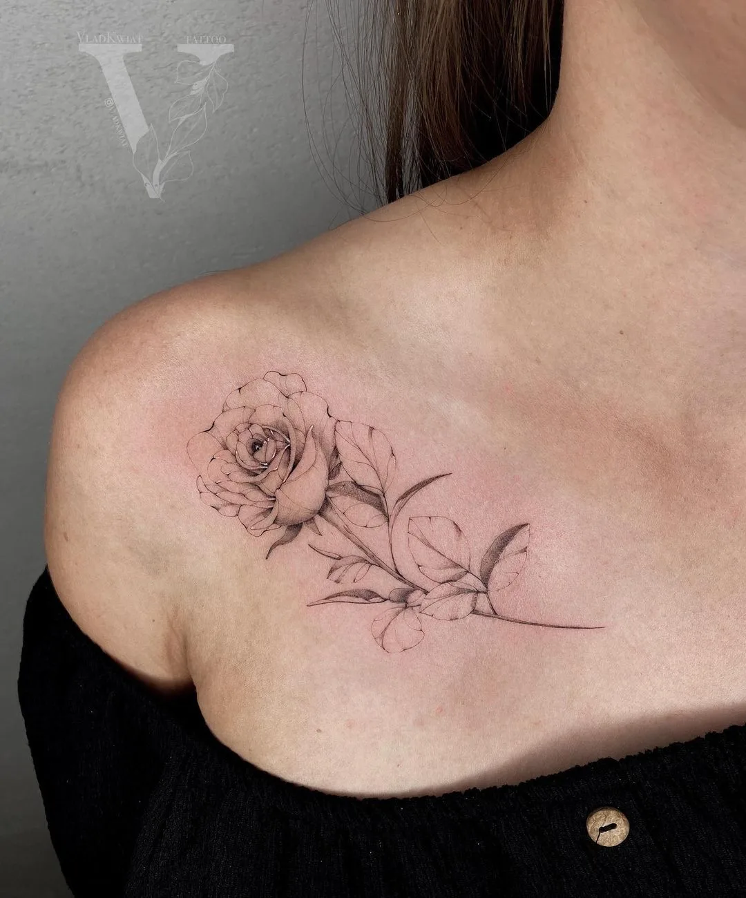 Ein zartes Schwarz-Grau-Rosen-Tattoo mit Blättern entlang des Schlüsselbeins platziert.