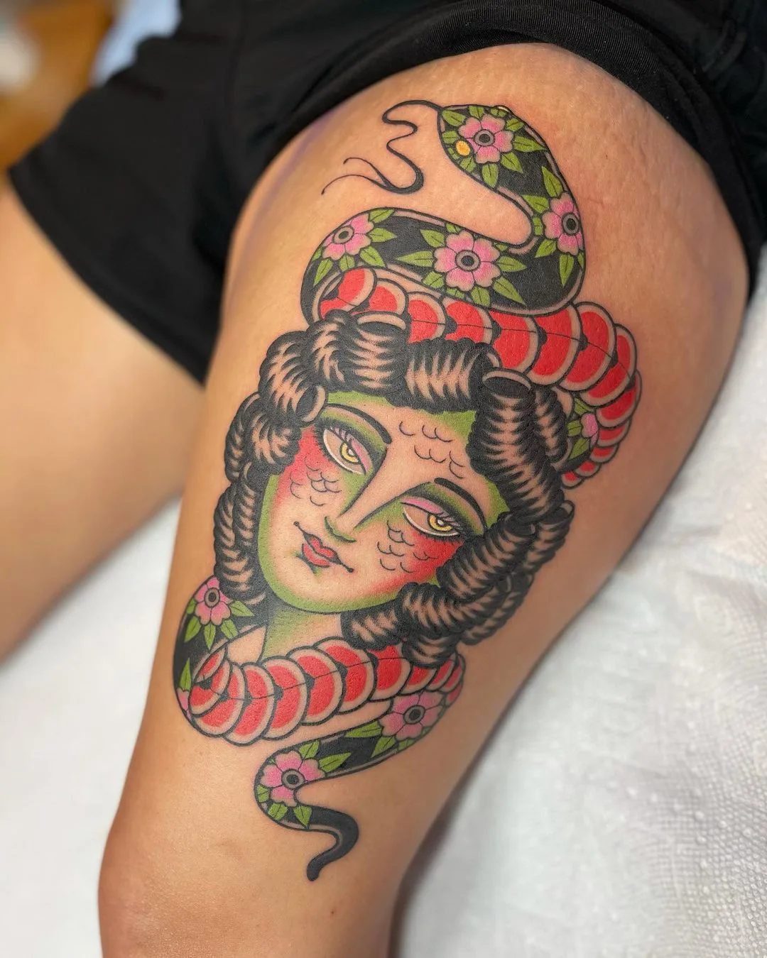 A neo-traditional tattoo featuring a woman's face with a snake coiled around her head, rendered with rich colour and detailed linework.
