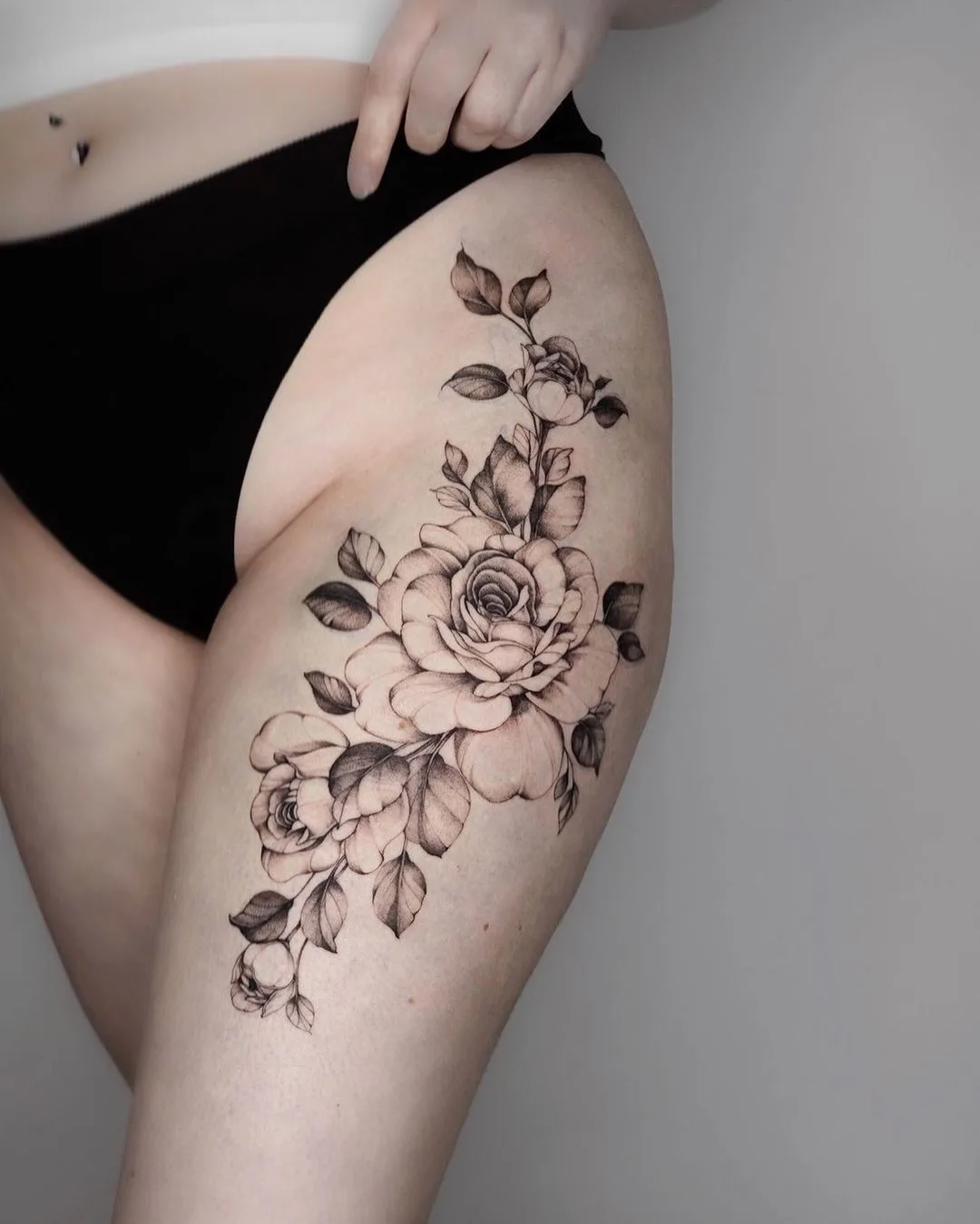 Ein detailliertes Schwarz-Grau-Tattoo von Rosen und Blättern im Fineline-Stil auf dem Oberschenkel platziert.