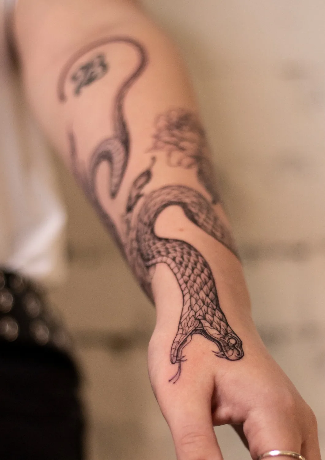 Tatouage en encre noire d'un serpent avec des écailles et une tête détaillée, placé sur l'avant-bras.